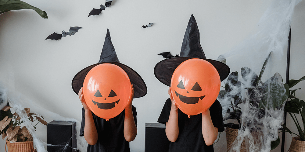Children dressed up as witches holding jack-o-lantern balloons to cover their face